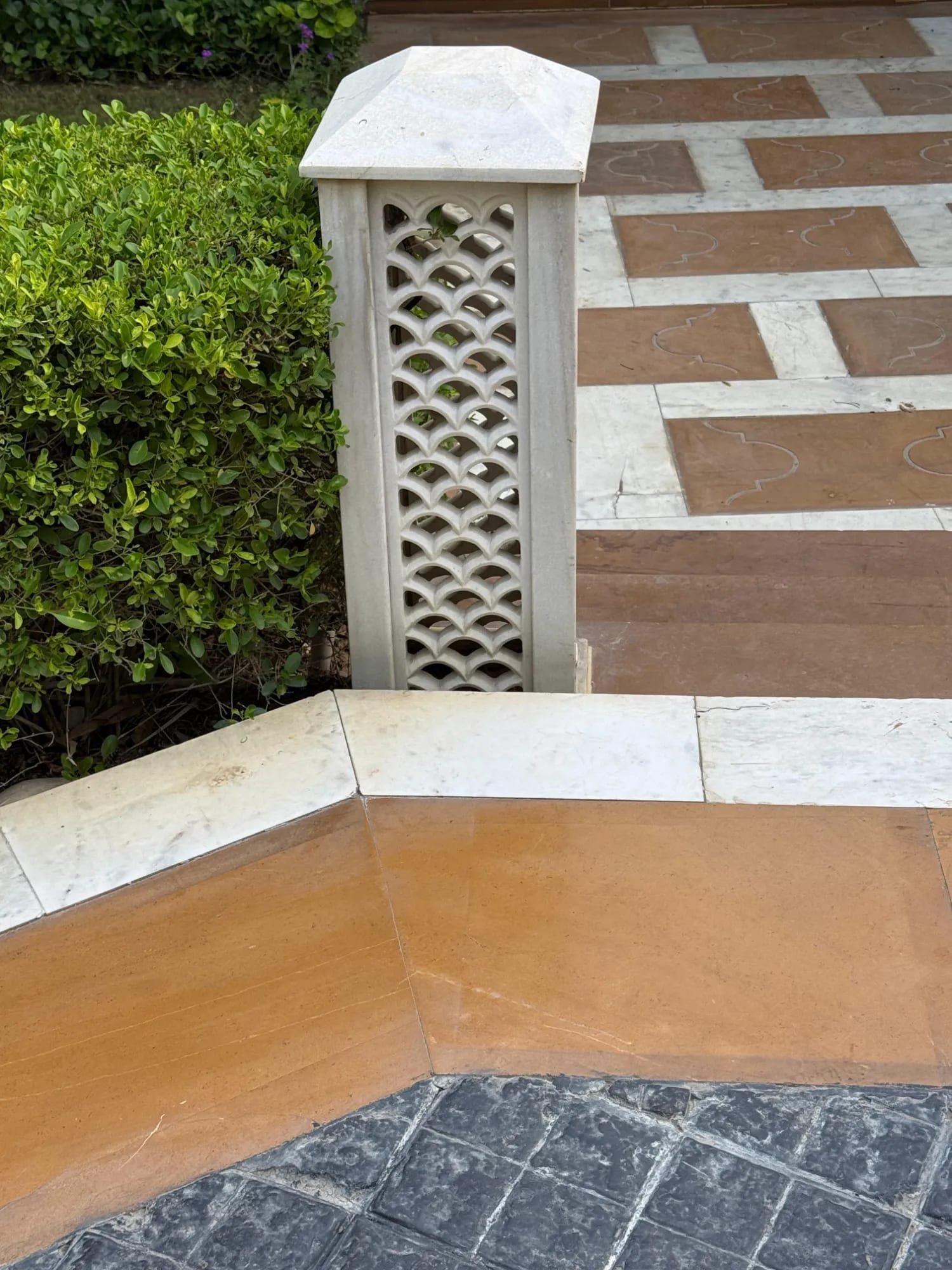 White marble scalloped jali gate pillar in a landscaped setting